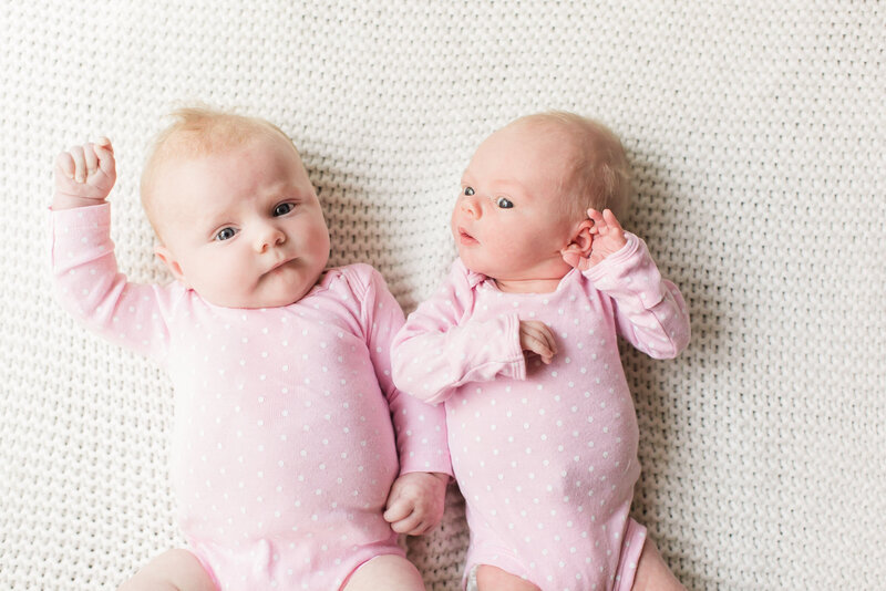 Two babies wearing pink onesies