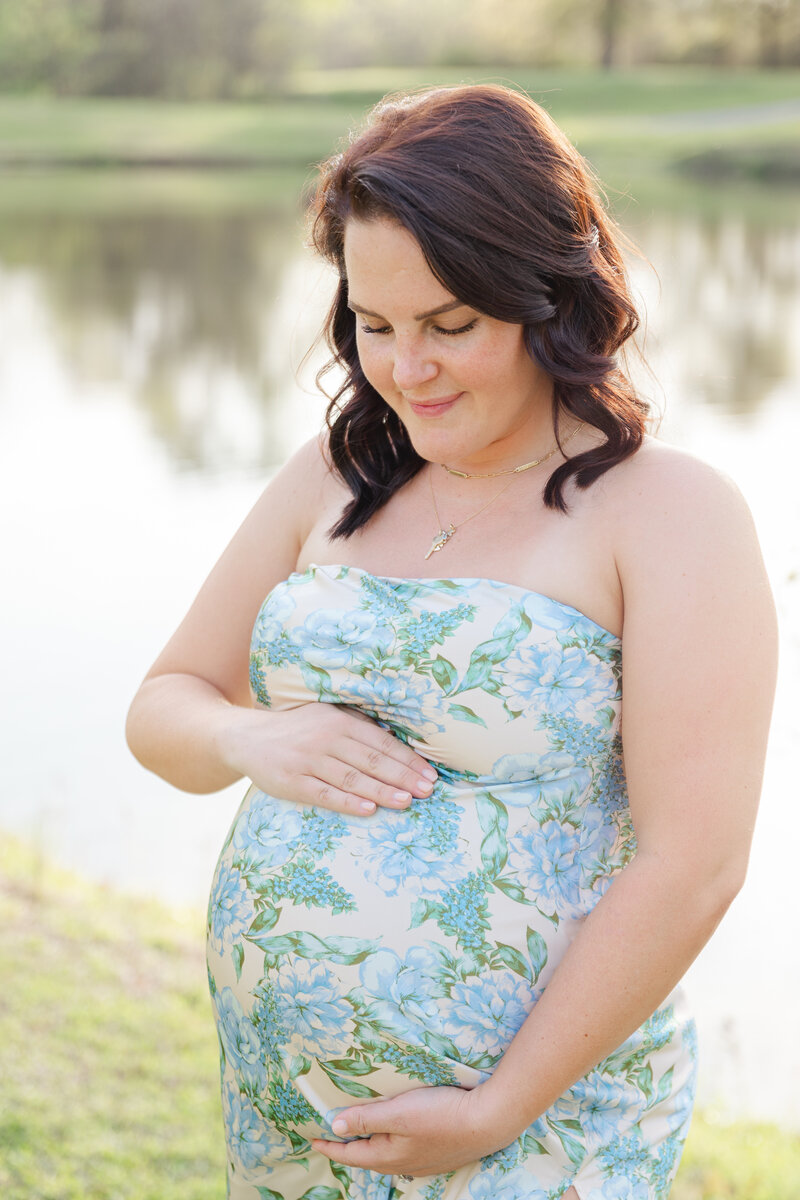 Pregnant woman cradles her belly while looking down and smiling.