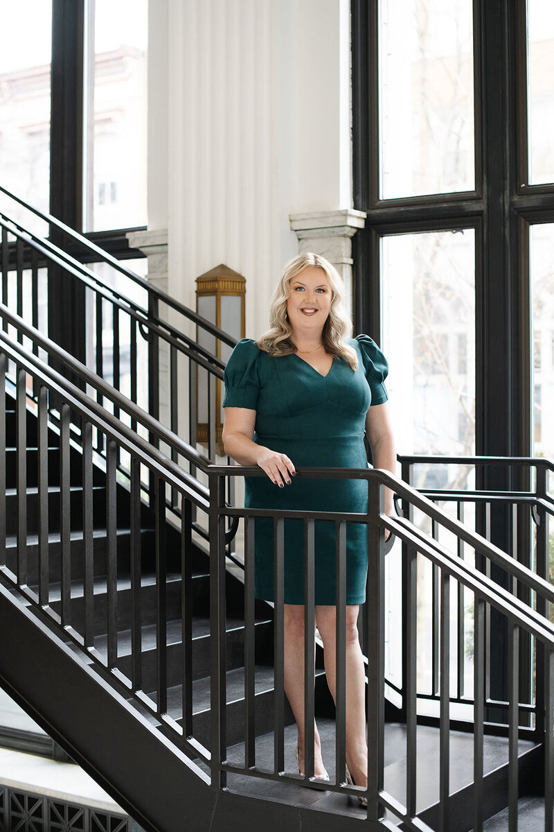 Career coach, Melissa Lawrence, stands on a staircase and smiles while holding the rail