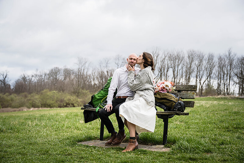 A nonbinary wedding couple sit on a bench inside of a greenhouse in Cave Springs, Virginia for a portrait on their elopement day.