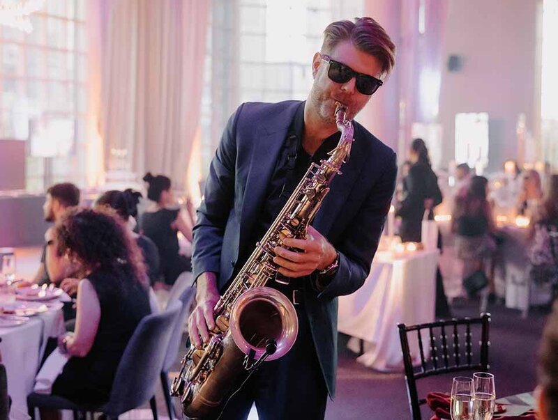 Live saxophone player performing at a formal indoor wedding with guests dining in the background.