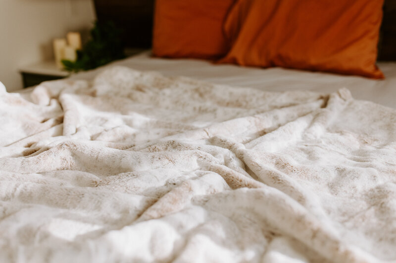 a white blanked laying on a bed with red pillows on it