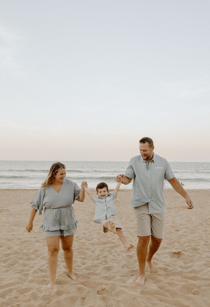 Couple holds onto their son's hands and lift him into the air as they are walking