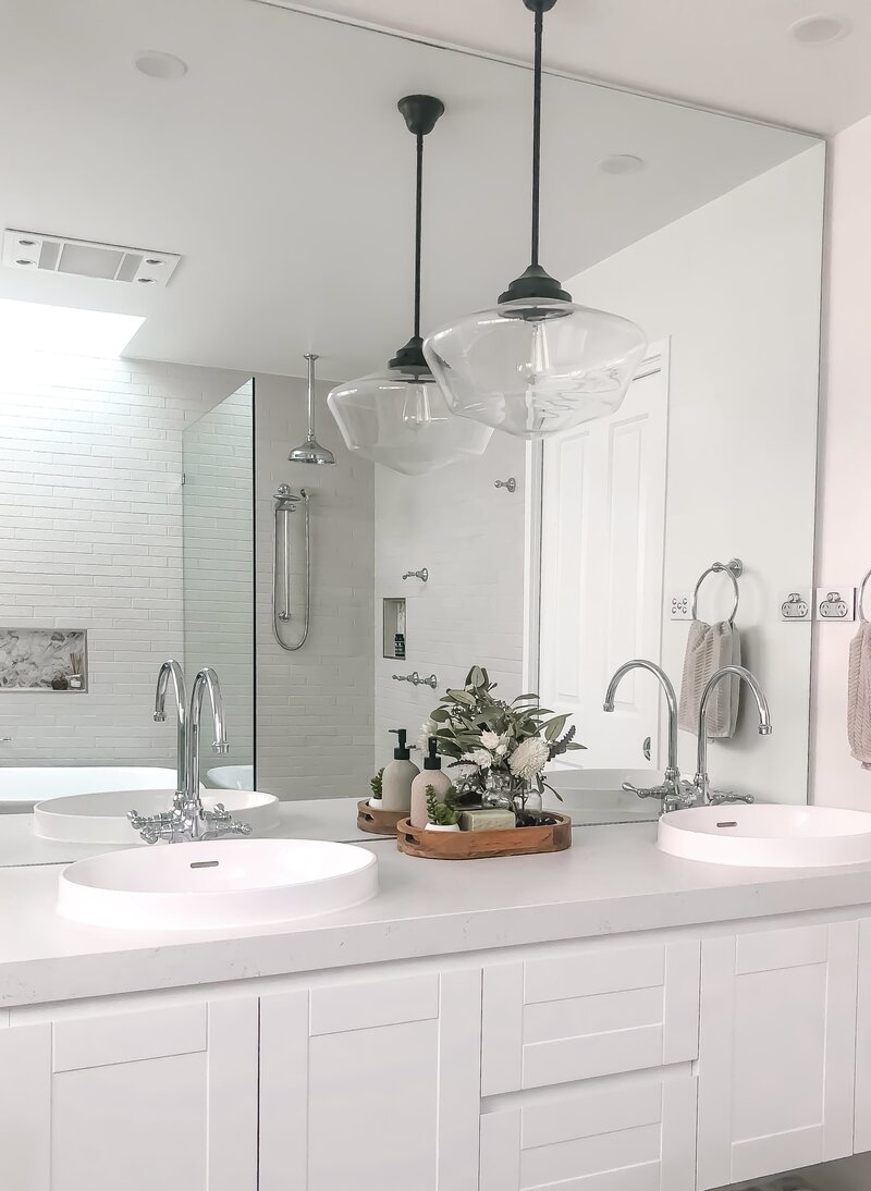 Modern bathroom with double sinks, a large mirror, pendant lights, and a tray with plants and toiletries. This space exemplifies luxury home design in Newcastle, combining elegance with functionality for the discerning homeowner.