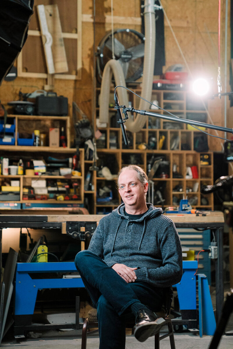 a man being interviewed sits under a boom microphone smiling