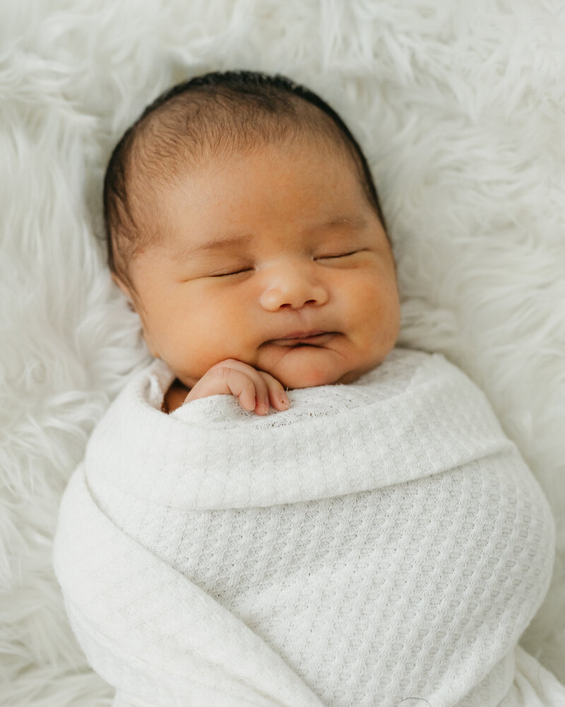 Small baby boy wrapped in a white swaddle in white fur