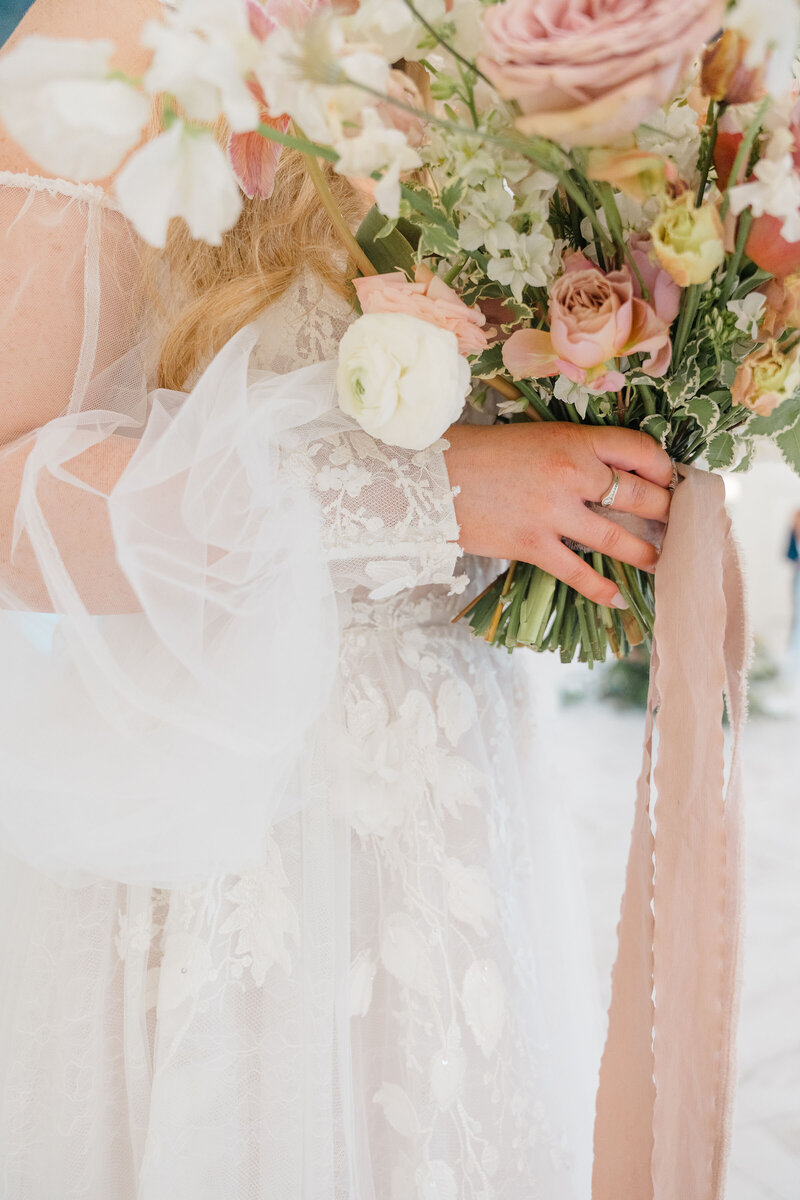 Bride holding pastel bouquet with lace dress details.