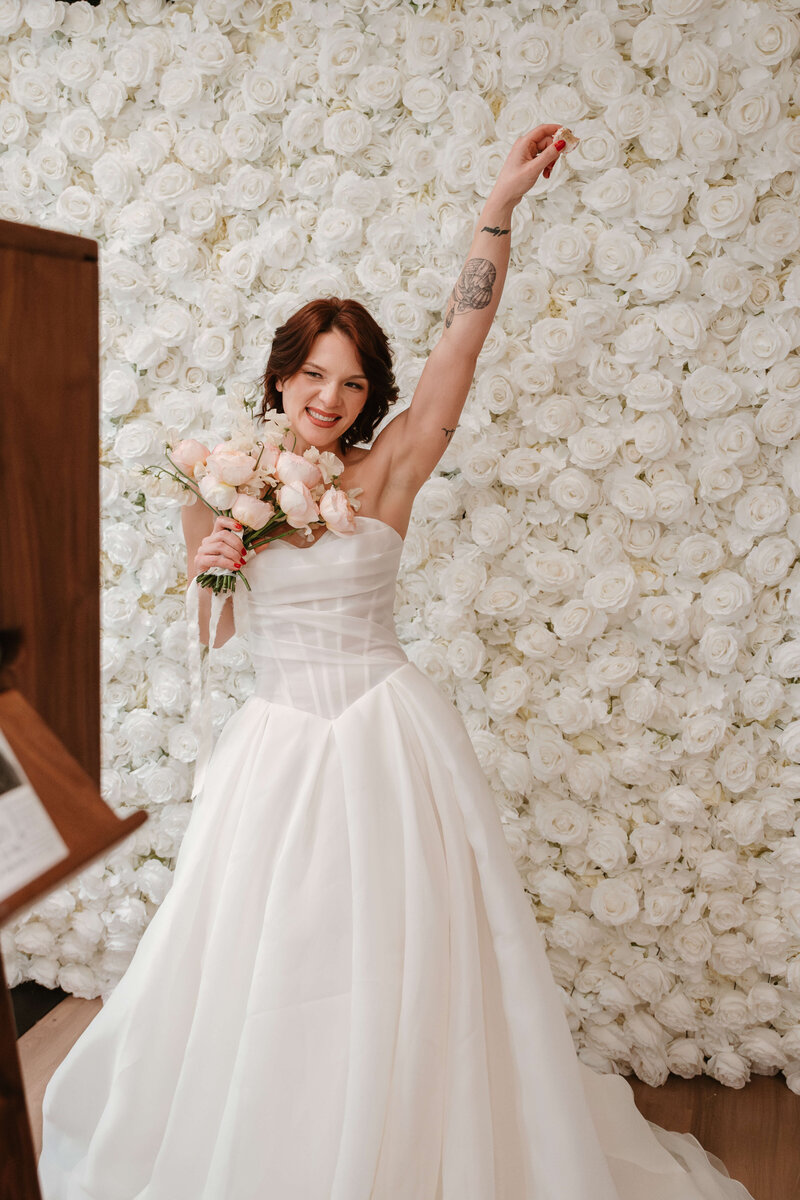 A premium photo booth backdrop with white roses and a bride holding her bouquet and smiling in front of it.  r