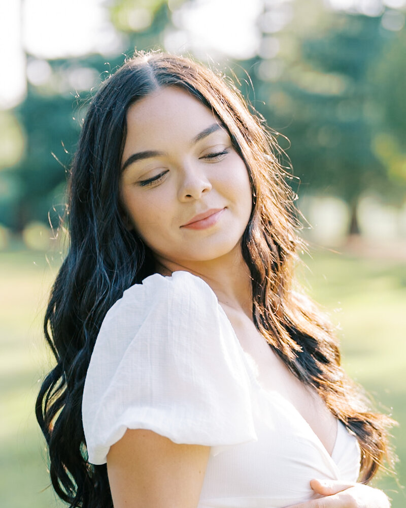 headshot of woman with dark hair and white dress on a sunny day in the park