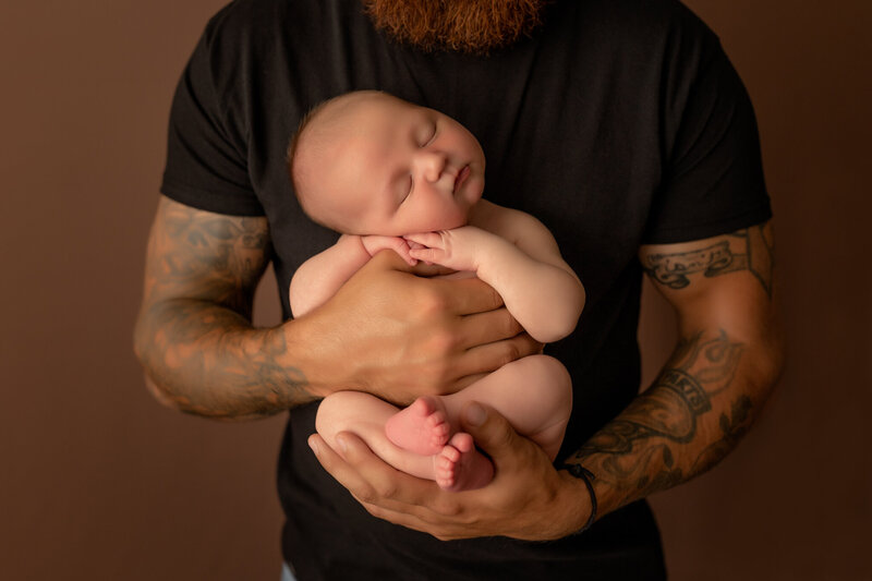 dad with tattoos holding newborn baby in studio