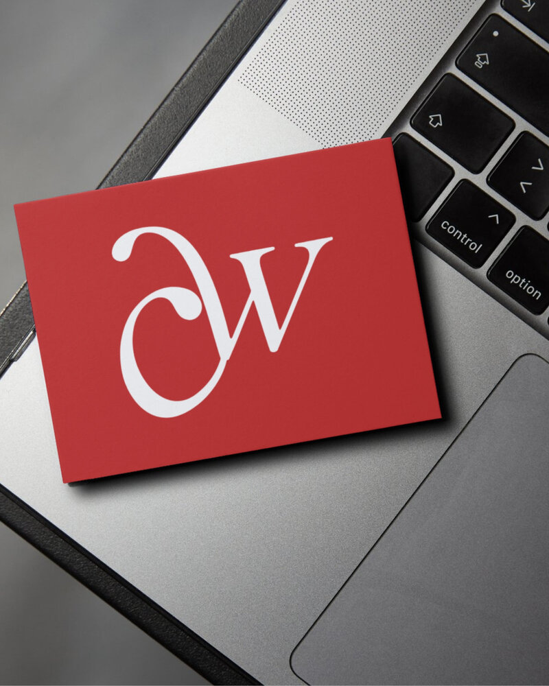 Red business card with a white “CW” monogram logo placed on a laptop keyboard.