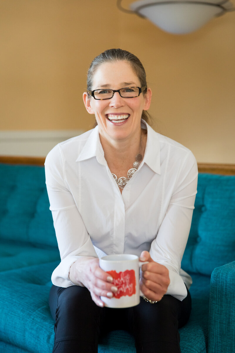woman sitting on a couch smiling while holding a mug