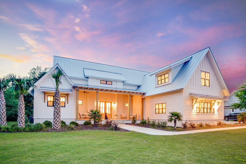 A stunning front view of a white barn-style mansion set against a breathtaking purple and pink sky. The image captures the elegance and charm of the property, enhanced by the beautiful sunset backdrop.