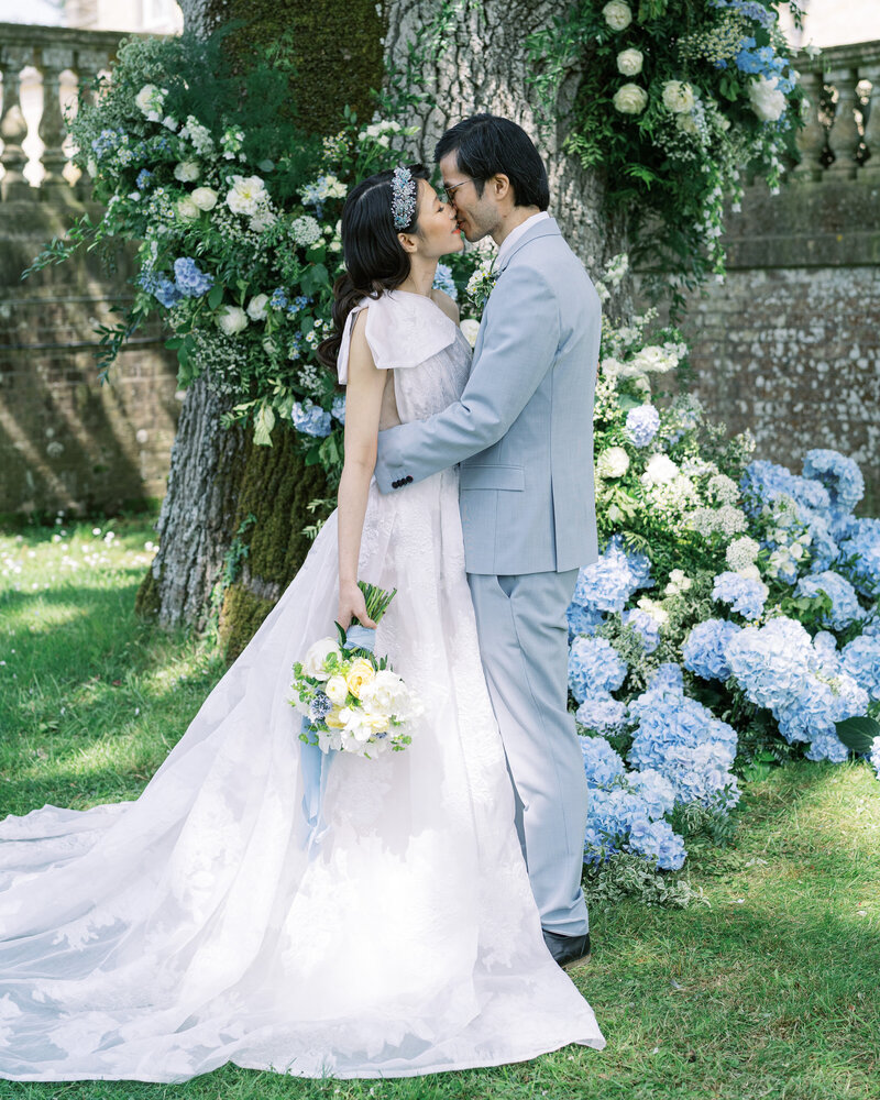 Bride and groom kissing in front of floral tree at their wedding ceremony at Somerley House wedding venue