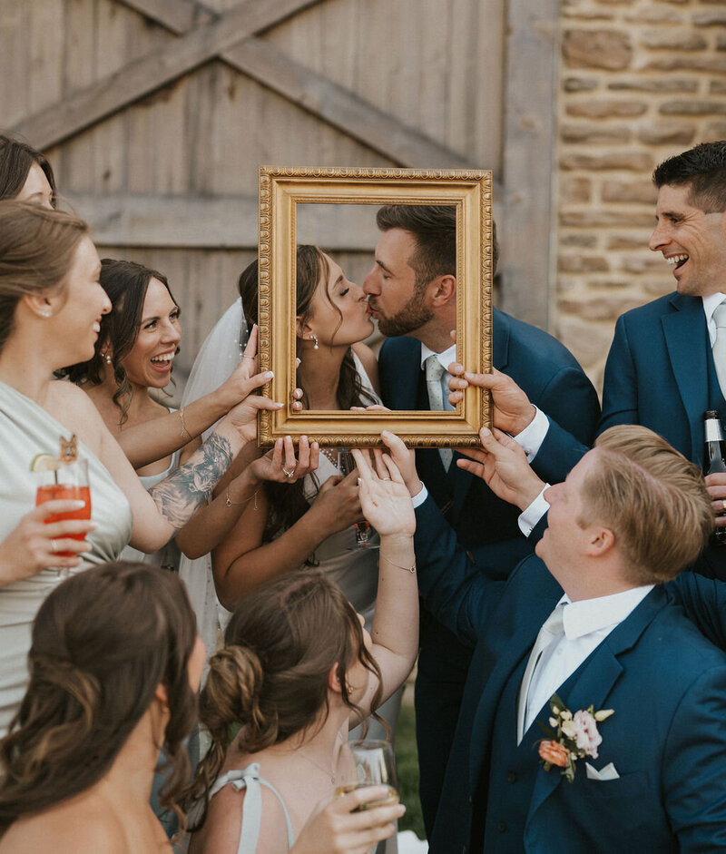 Bride and groom kissing while their wedding party holds an empty picture frame around them during a fun NYC wedding photo