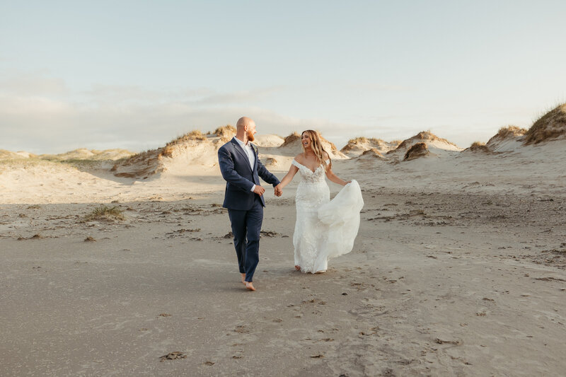 Bride and groom walking barefoot in the sand on the beach
