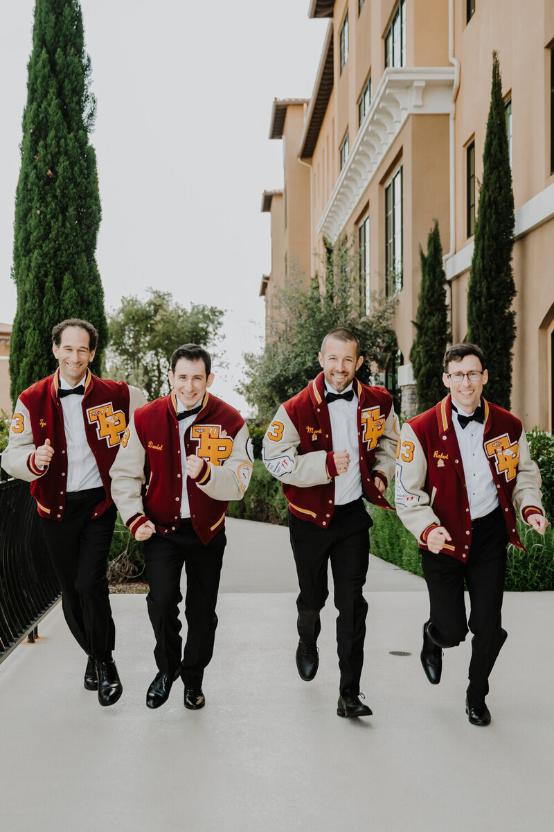groomsmen laughing while wearing lettered jackets
