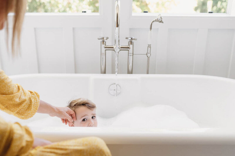 little boy peering out of a bathtub with his mom touching his face in their McLean, VA home