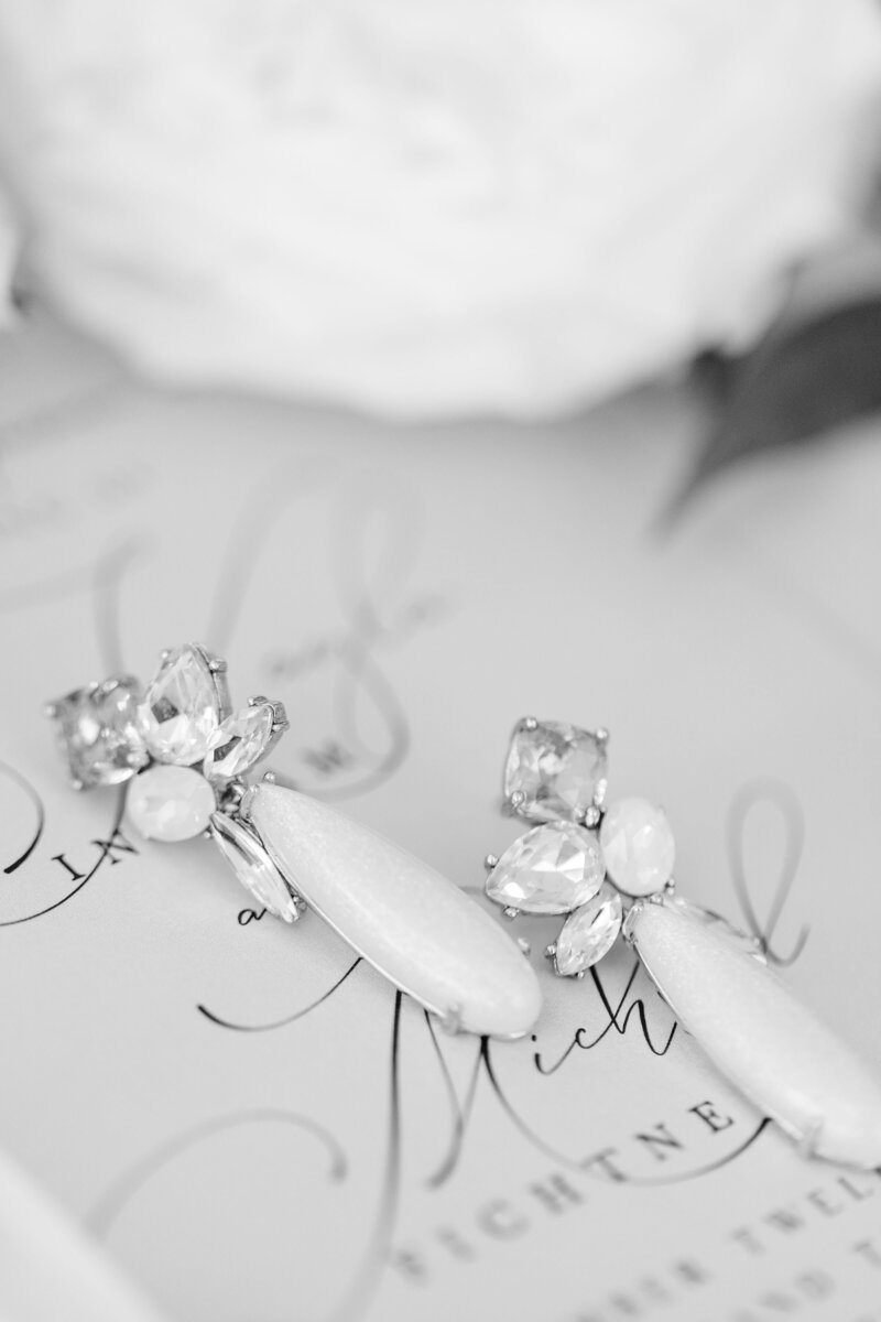 bride earrings on top of wedding invitation in black and white