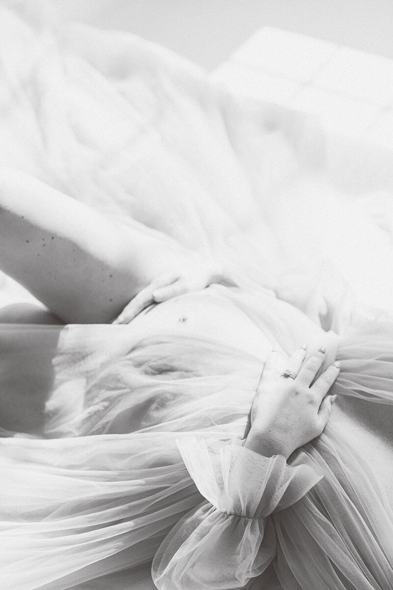 Black and white detail of a maternity dress with a woman's hands gently resting on her belly.