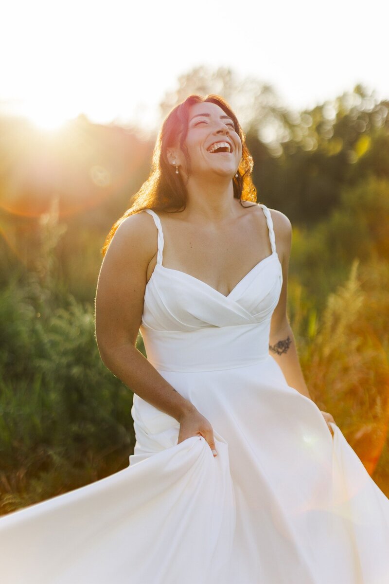 Bride laughing with her head tilted back in golden hour light as her dress moves around her