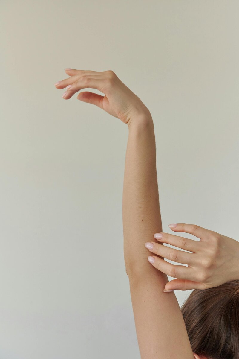 Brunette woman holding arm overhead against a neutral colored wall