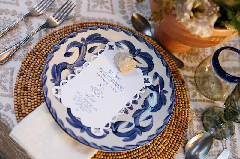 Close-up of Mexican-inspired wedding place setting with blue and white Talavera-style plate, custom die-cut menu, and woven charger, styled by Eventive Designs.