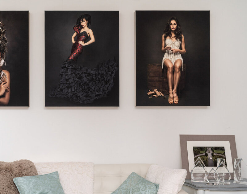 room with couch, pillows, and portraits of elegantly dressed lady in dark studio backgrounds