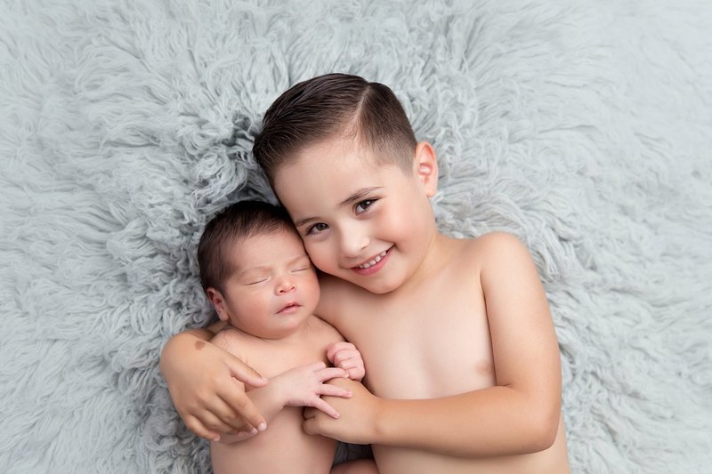 sibling boy holding little brother on blue grey flokati