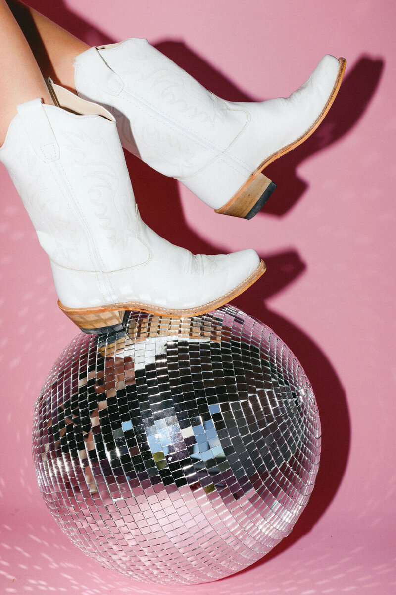 White cowboy boots on a disco ball in front of a pink background
