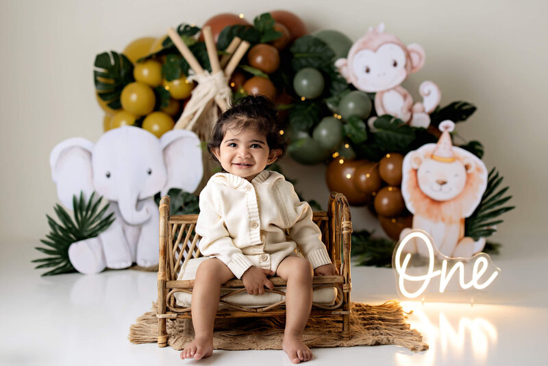 Toddler boy sitting in front of a jungle theme backdrop smiling at the camera.