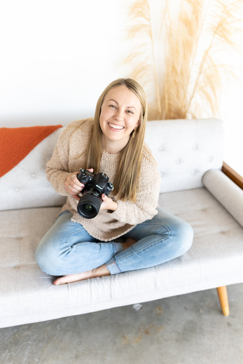 Photographer sitting on couch while smiling holding her camera