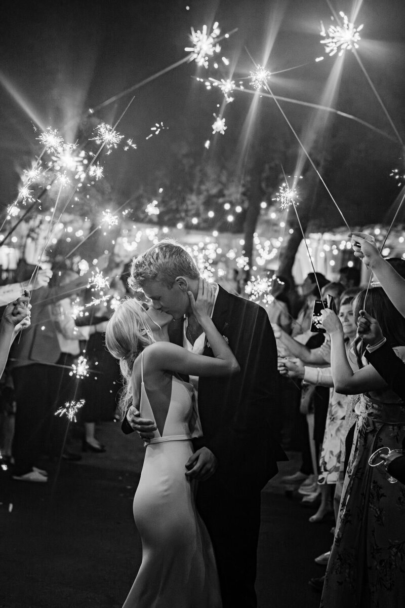Bride and groom share a passionate kiss during a magical sparkler exit at their luxury wedding in Sea Pines, Hilton Head. A timeless black-and-white celebration under glowing lights.