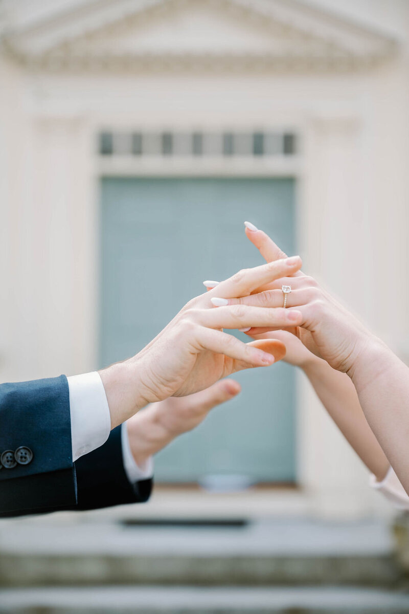 Wedding Photographer RI | A close-up of two hands reaching towards each other in front of a blurred background of an elegant building. 