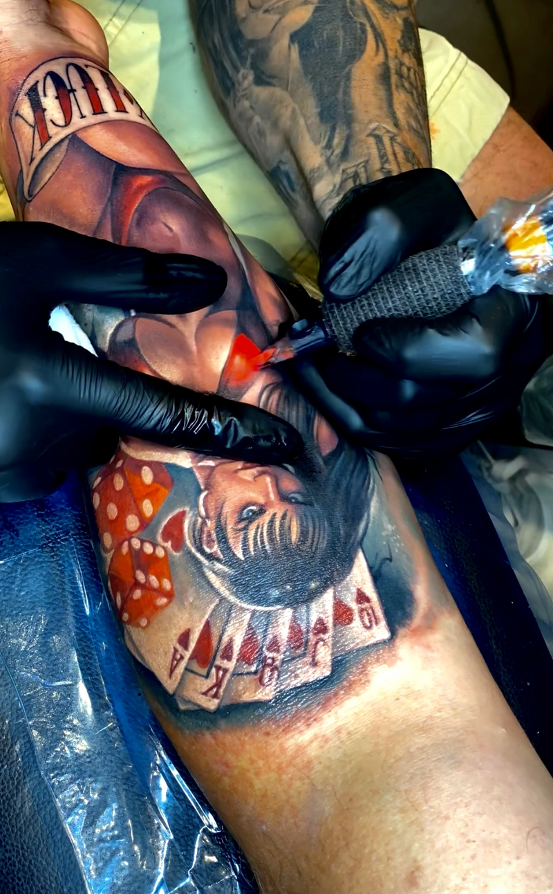 A colorful tattoo of a girl in a bikini surrounded by playing cards and dice, blending pin-up style with gambling-themed elements.