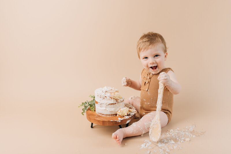 One-year old boy at his first year cake smash portrait session, smiling at the camera