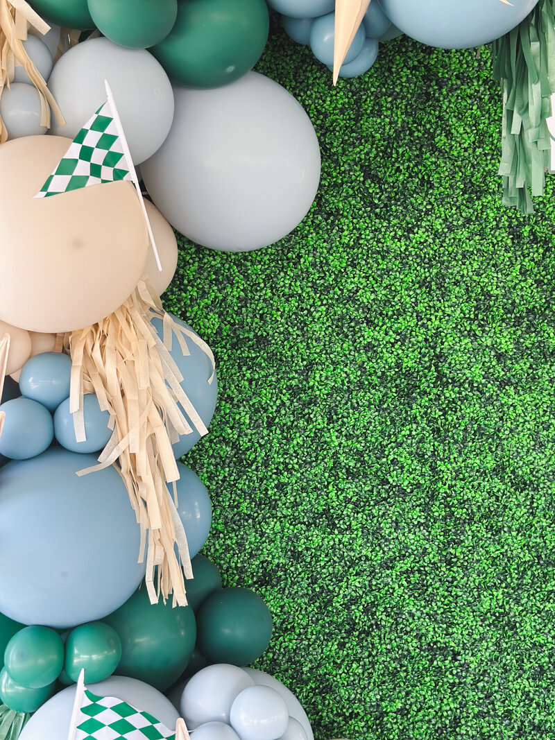 Balloon garland with blue, tan, and green decorations and a golf checkered flag.