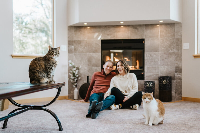 Jen and Mark Heller with their cats in front of a fireplace