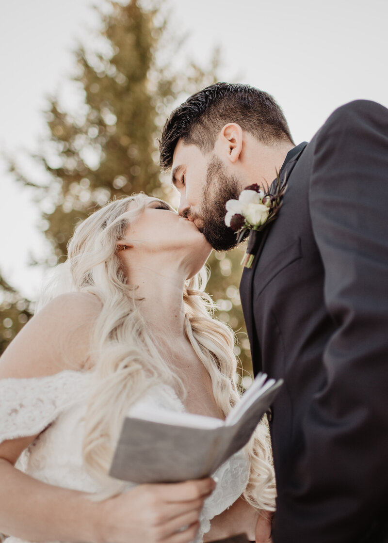 bride and groom kissing as the bride holds a grey vow book for a winter grand teton wedding captured by photographers Jackson Hole