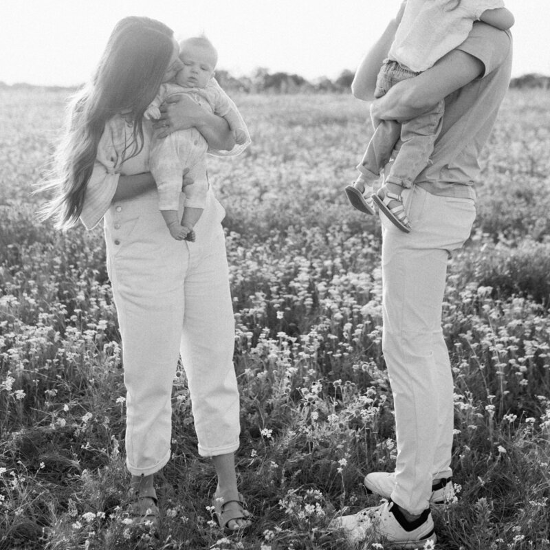 Black and white image of mom and dad holding their two small children in a grassy flower field