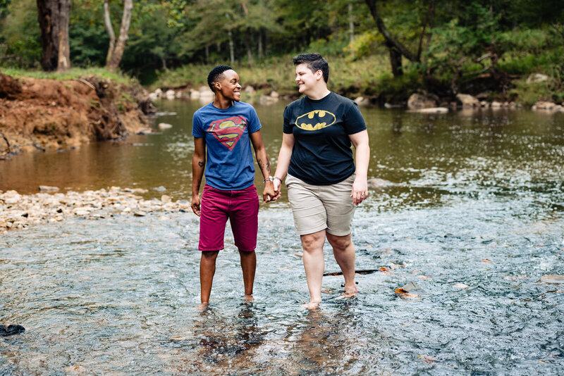 Two women hold hands and wade through the Eno River during their engagement photo session.