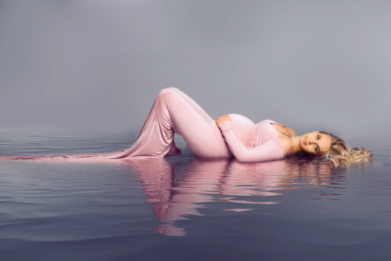 Elegant maternity portrait of an expectant mother in a flowing pink gown, captured with a serene water reflection effect in Overland Park, Kansas. A perfect example of creative maternity photography for families in the Kansas City metro area.