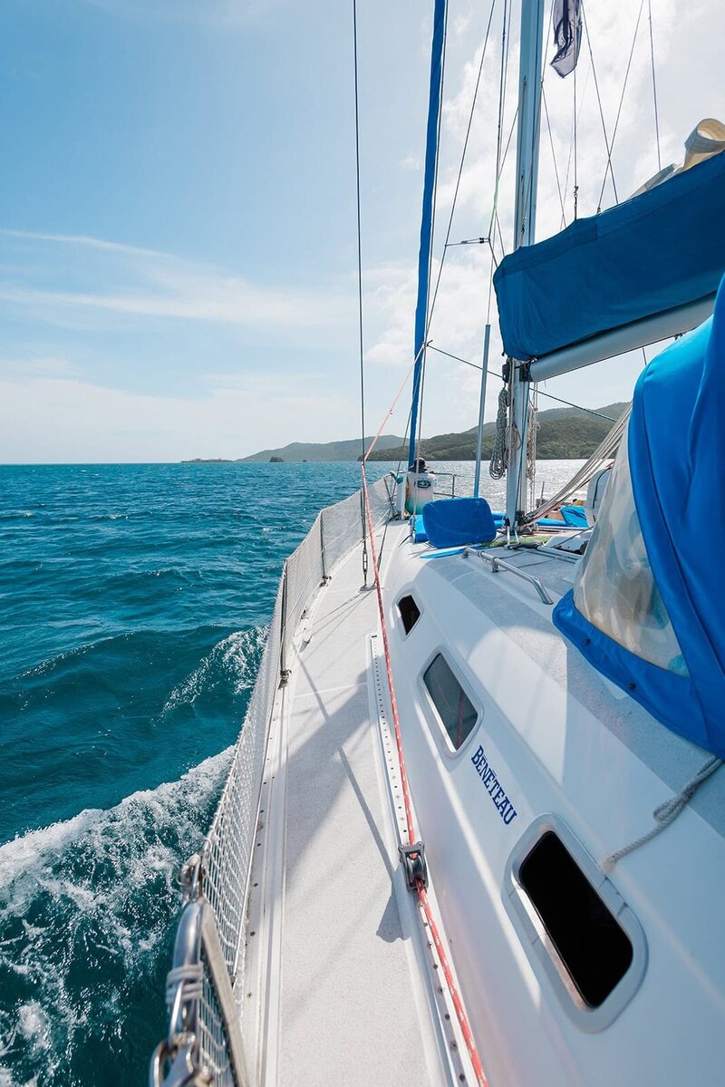 The bright white and blue of a liveaboard sailing boat in the beautiful blue sea of Greece during an adventure luxe wedding with a luxury elopement photographer.  The sky is beautiful blue also, with light haze of white clouds. 