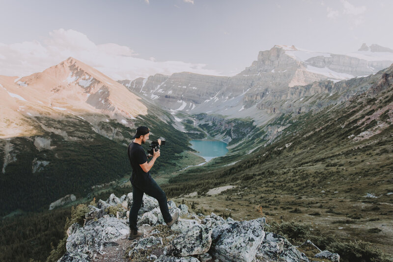 Matt shown standing on a rock overlooking a beautiful mountain valley filming a couple on their wedding day in banff