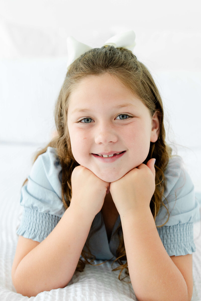 Girl sitting with hands under chin smiling at camera for milestone photos in mini model rep program