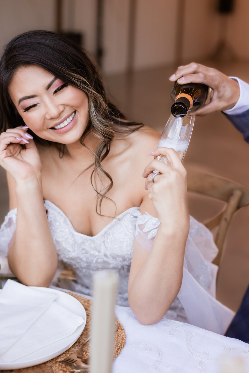 A bride being poured more champagne by her groom. Maybe just onneeeeeeee more.