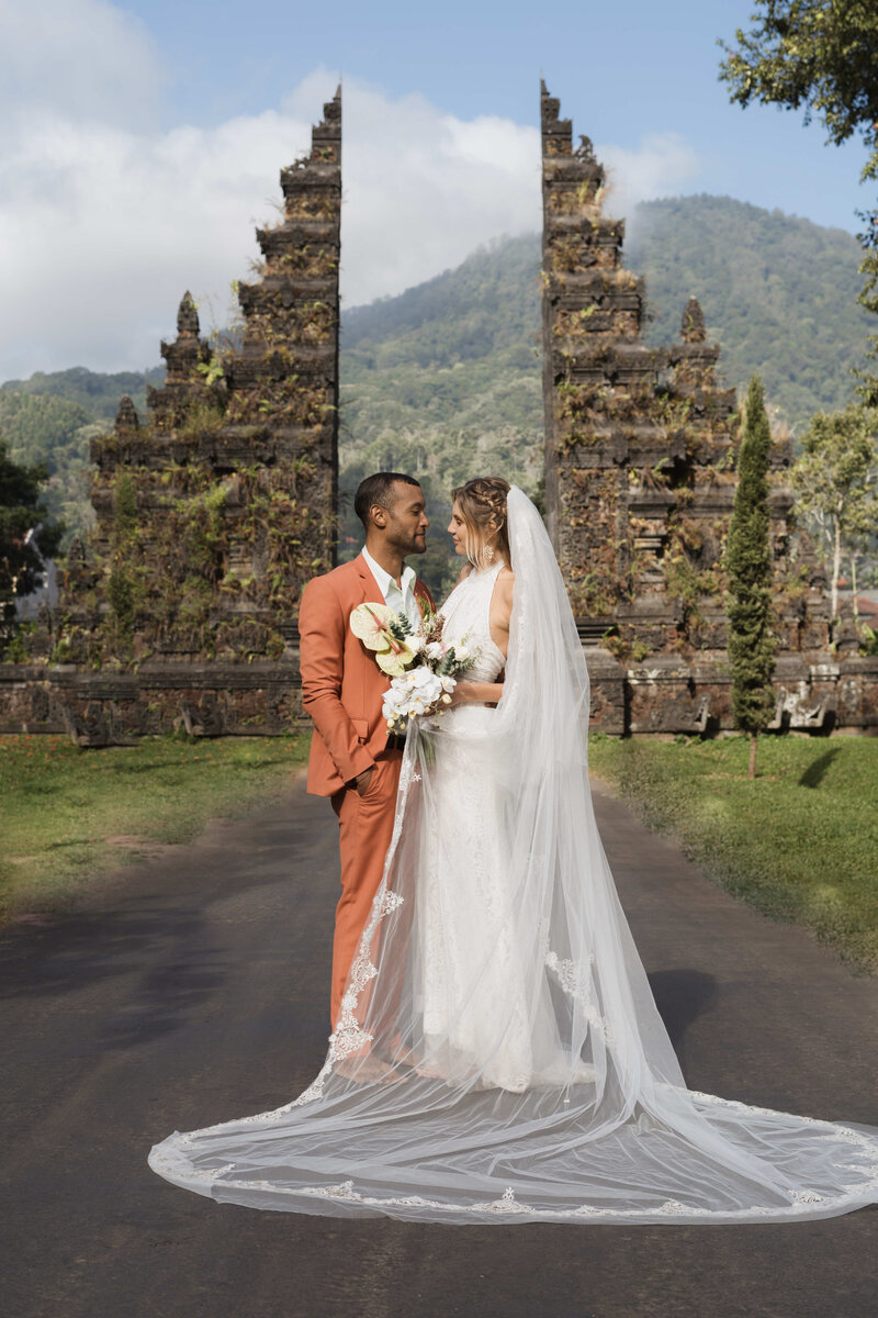 bride and groom stand together on cliff by water in Bali