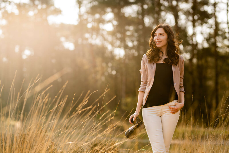 Natascha houdt de camera vast in haar rechter hand en kijkt opzij terwijl haar andere hand rust in haar broekzak in de Ginkelse Heide