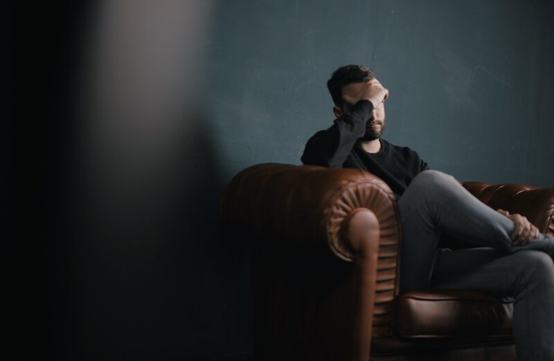 Man with anxiety sitting on a couch during therapy with his head in his hands