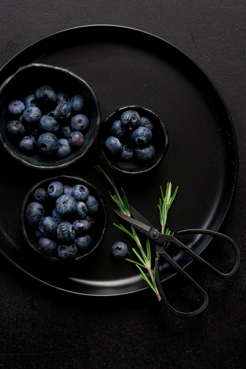 Blauwe bessen op een zwart bord met rozemarijn en een zwarte schaar. Foodfoto dark en moody style. Dorien Paymans  Fotograaf Groningen | studio Ensō ©